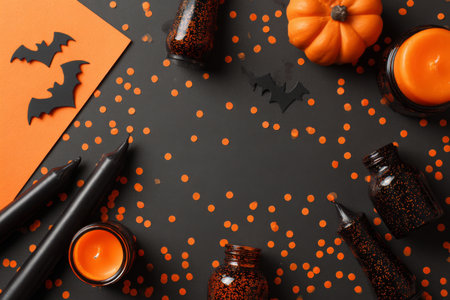 Bright orange pumpkin and black candles are surrounded by bat cutouts and confetti, creating a festive Halloween display on a dark surface in autumn.の素材