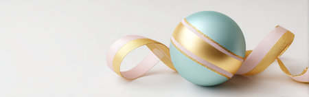 A beautifully crafted pastel ornament in light blue rests on a smooth surface. It features shiny gold and pink ribbons artistically wrapped around it, creating a festive atmosphere.の素材