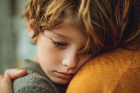 A young child embraces an adult, resting their head on their shoulder. The moment reflects warmth and affection, set in a softly lit area, emphasizing the bond they share.の素材