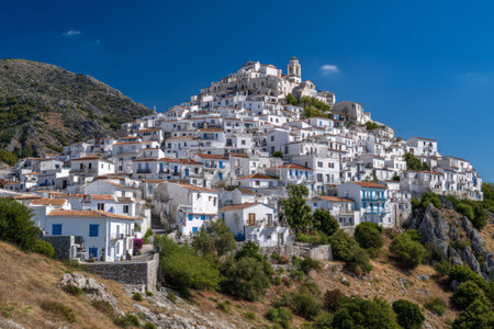 A stunning village perched on a hillside showcases white houses against a backdrop of mountains and a vibrant blue sky. The scene invites exploration and relaxation.の素材