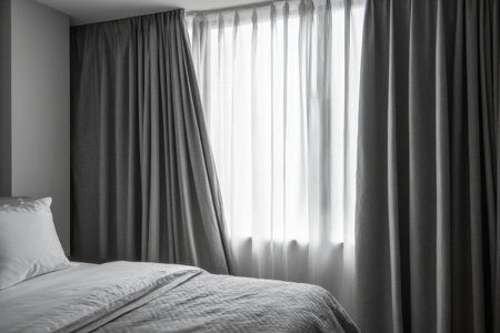 Soft light streams through sheer curtains in a cozy bedroom. The bed is neatly made, creating a serene and inviting atmosphere for relaxation and rest.の素材