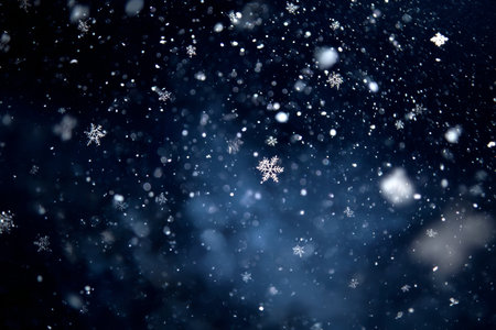 Delicate snowflakes drift down softly against a dark blue night sky. The scene captures the beauty of winter as flurries swirl in the cold air, enchanting viewers with its tranquility.の素材