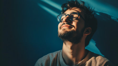 A young man sits in a cozy indoor space, basking in warm sunlight filtering through a window, showcasing a moment of serene contentment and joy.の素材