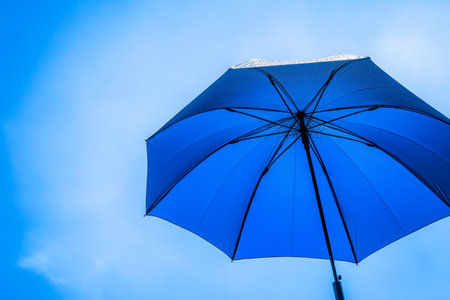 A vibrant blue umbrella stands out against a bright, clear sky, showing a perfect blend of color and tranquility on a sunny day. This visual captures comfort and joy.の素材