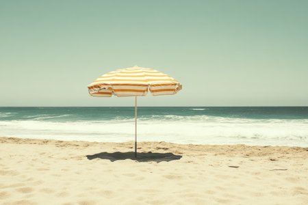 A yellow and white striped umbrella is positioned on the sandy beach, providing shade as gentle waves roll in. The scene captures a tranquil moment by the shoreline.の素材