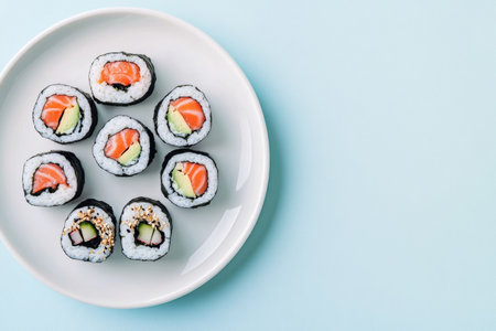 Sushi rolls with fresh ingredients are presented on a pristine white plate, creating a beautiful contrast against a soft light blue backdrop, showing colors and textures of the food.の素材