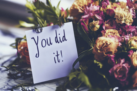 Handwritten note expresses congratulations with the words you did it placed beside a vibrant bouquet of flowers in a warm indoor setting during daylight hoursの素材