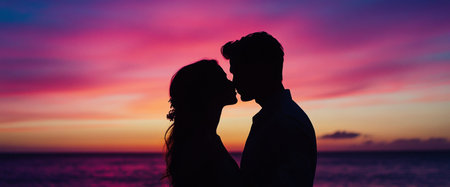 A couple stands close together against a vibrant sunset sky, sharing an intimate kiss. The ocean reflects the colorful hues, creating a serene atmosphere.の素材