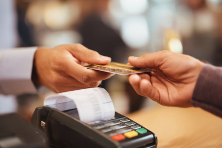 A customer hands their credit card to the cashier at a cafe. The surroundings are lively with soft lighting and other patrons chatting. It is an afternoon setting.の素材