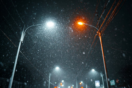 Heavy snow falls silently in a dark urban area, illuminated by warm orange and cool white streetlights. The scene captures the peacefulness of a winter night.の素材