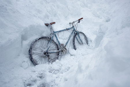 A blue bicycle is partially buried in thick snow along a narrow path created by snow removal in a residential neighborhood. The scene captures the aftermath of a heavy winter storm.の素材