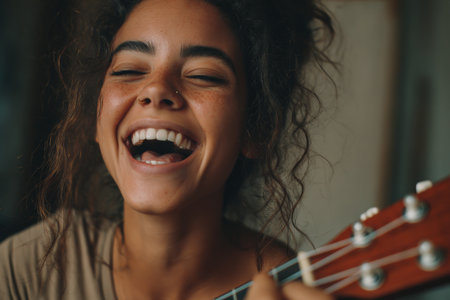 A young woman with curly hair is laughing while playing a guitar in a warm, inviting indoor space. Her happiness is evident as she enjoys the moment of music and joy.の素材