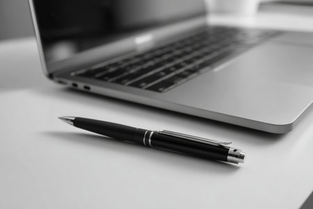 A black pen rests next to a silver laptop on a minimalistic desk. Natural light shines on the setup, creating a calm working environment for focused tasks.の素材