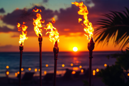 Tiki torches glow brightly along a tropical beach as the sun sets, casting vibrant orange hues across the sky and inviting guests to enjoy the evening festivities by the shore.の素材