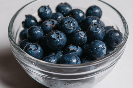 Close-up view features plump blueberries resting in a glass bowl, accentuated by glistening water droplets. This macro shot captures their vibrant color and texture beautifully.の素材