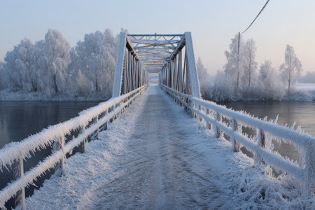 A serene scene shows a frosty bridge over a still river, with trees covered in ice. The soft light of morning creates a peaceful winter atmosphere.の素材