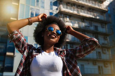 Positive emotions and people concept young black african american female with curly black hair. Over city background. Lifestyle.の写真素材