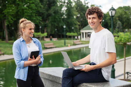 Image of happy couple people. Female and male in urban park in casual style, using technology for working and online education outdoor looking in laptop. Lifestyle.の写真素材