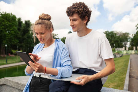 Image of happy couple people. Female and male in urban park in casual style, using technology for working and online education outdoor looking in laptop. Lifestyle.の写真素材