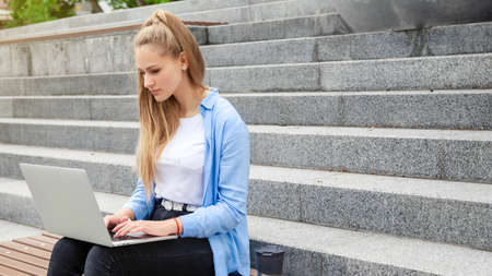 Dreamy and stylish European young student girl in wireless earphones wearing white t-shirt, writing to notebook at summer day.の写真素材