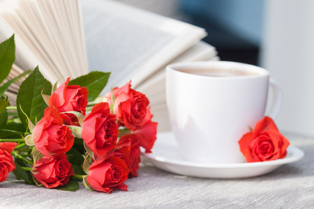 An open book with red orange roses and a cup of tea. Reading and relaxing. Romantic, sweet, dating concept.の写真素材