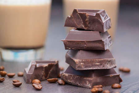 Pieces of dark chocolate, coffee beans and cups of cocoa or coffee with milk on wooden background.