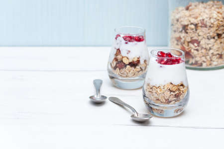 Homemade yougurt with granola and pomegranate fruit in glasses on white wooden table. Healthy breakfast.の写真素材
