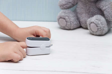 Pulse oximeter on kids finger for measure pulse rate and oxygen level on white wooden table. Healthy concept.の写真素材