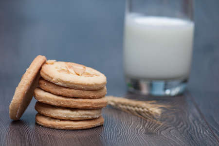 Tasty cookies biscuits with almond and wheat on the white plate on the wooden background. A glass of milk or yogurt with biscuits.の写真素材