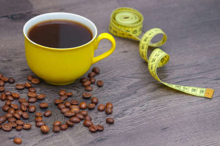 Yellow cup of coffee with beans and tape measure on wooden background.の写真素材