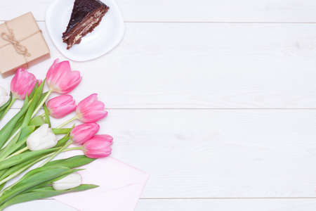 Bouquet of pink tulips, chocolate cake. pressent box on white wooden background. Copy space, close up. Mother's, women's day concept. Flat lay.の写真素材