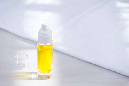 Glass botle with oil for hair or skin care with white towel. Sunlight, morning.