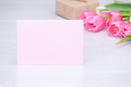 Spring pink tulips, gift box and empty paper card on white wooden background. Mother's, Women's Day concept.の写真素材