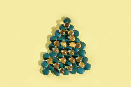 Supplements and vitamins in shape of christmas tree on yellow background, copy space.の写真素材