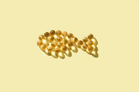Fish oil capsules in the shape of fish on yellow background, copy space.の写真素材