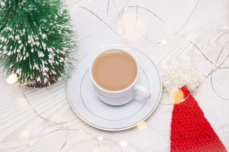Cup of coffee with milk near christmas tree and santa hat.の写真素材