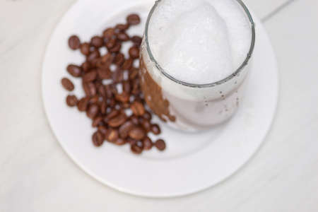 Glass coffee with foam milk with honey on white wooden table.