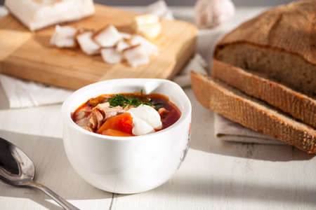 Traditional Ukrainian borscht. Red beet roof soup with homemade bread on white wooden table.