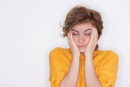 An unhappy, exhausted girl with closed eyes, touches her temples in close-up, a tired woman suffers from a headache or migraine, does not feel well, suffers from insomnia, lack of sleepの写真素材