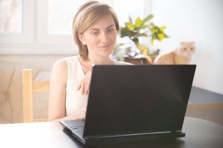 A woman in home clothes works on a computer in front of a monitor in a home atmosphere. Flexible working hours and remote work.の写真素材