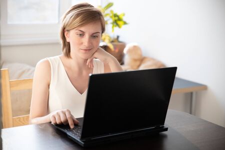 A woman in home clothes works on a computer in front of a monitor in a home atmosphere. Flexible working hours and remote work.の写真素材