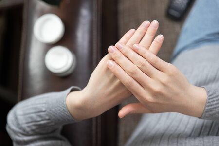 Cropped image of beautiful young woman applying cream while sitting on bed at homeの写真素材