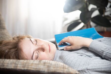 Beautiful young girl sleeping on the couch in the living room, she was reading a bookの写真素材