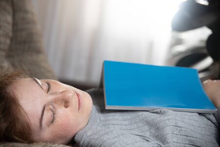 Beautiful young girl sleeping on the couch in the living room, she was reading a bookの写真素材