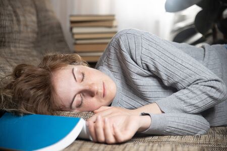 Beautiful young girl sleeping on the couch in the living room, she was reading a bookの写真素材