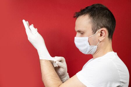 Professional medic in protective mask on face putting on blue latex gloves on hands. Young man surgeon in face mask wearing sterile medical glove. Medical examination in hospital. Coronavirus COVID-19の写真素材