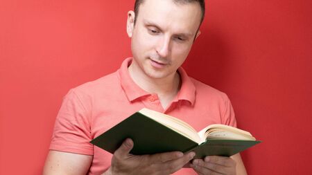 A smiling young stylish student stands with books on a clear red background in a casual bright top, pointing to the copy spaceの写真素材