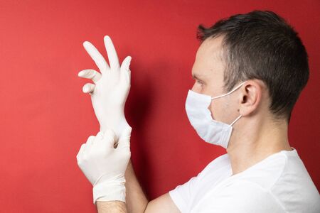 Professional medic in protective mask on face putting on blue latex gloves on hands. Young man surgeon in face mask wearing sterile medical glove. Medical examination in hospital. Coronavirus COVID-19の写真素材