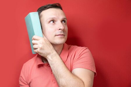 A smiling young stylish student stands with books on a clear red background in a casual bright top, pointing to the copy spaceの写真素材