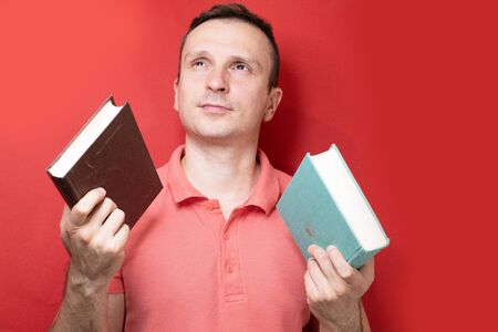 A smiling young stylish student stands with books on a clear red background in a casual bright top, pointing to the copy spaceの写真素材